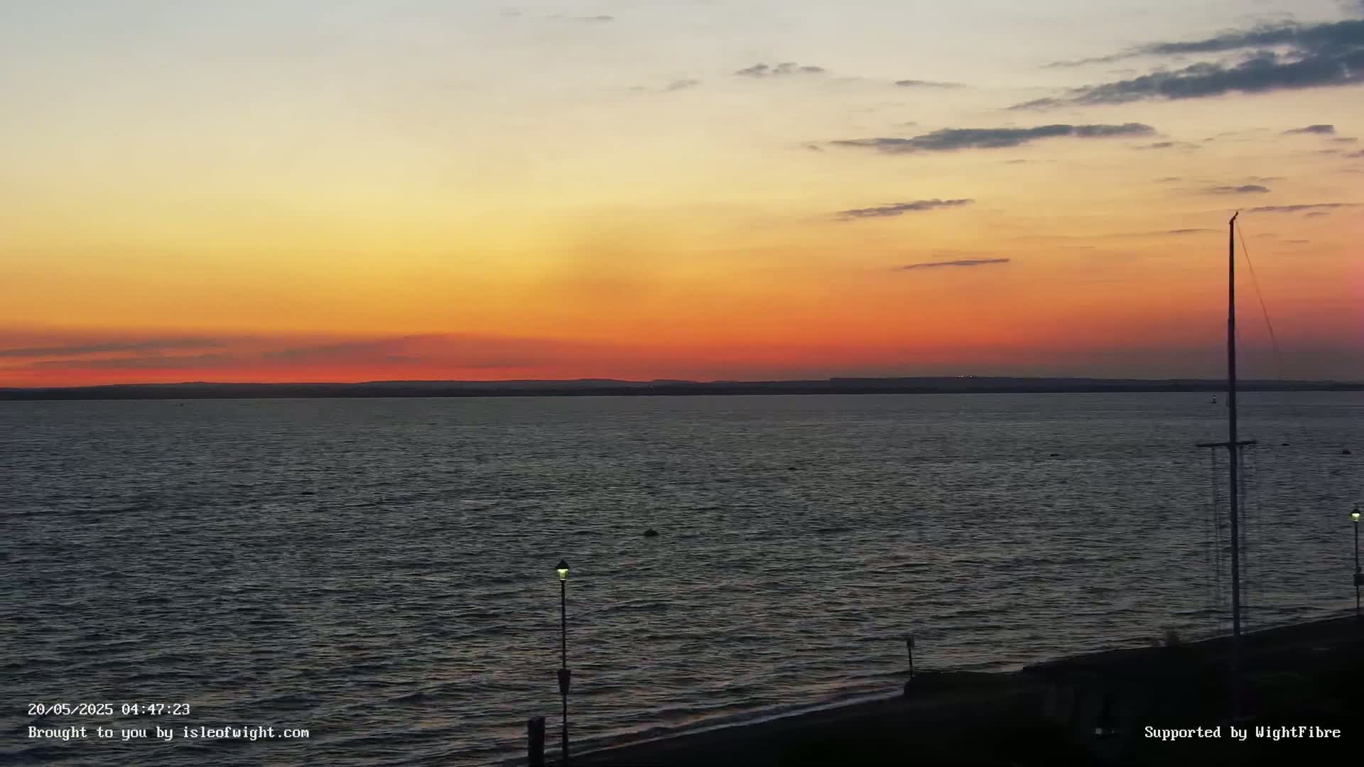 A calm body of water stretches to a distant shoreline under a vibrant sunset sky with orange and red hues.