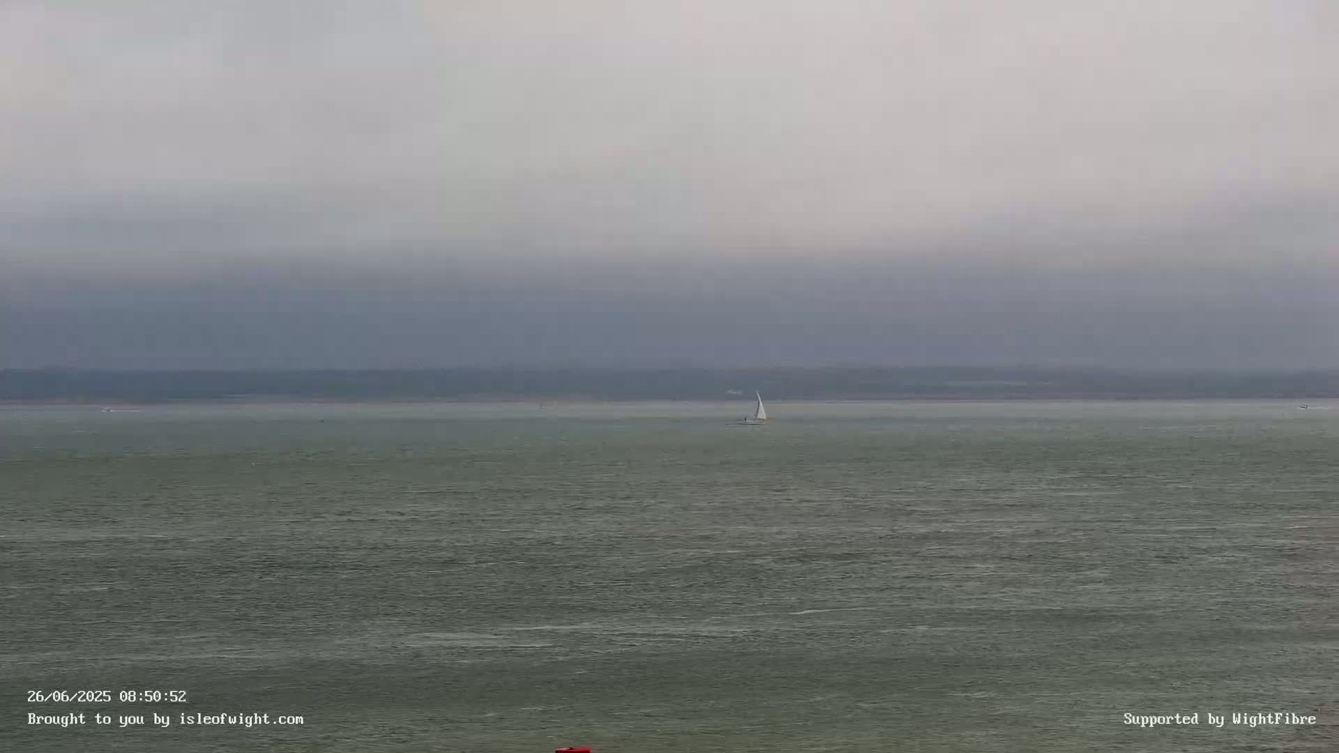 A sailboat is visible on a calm, gray sea under an overcast sky.