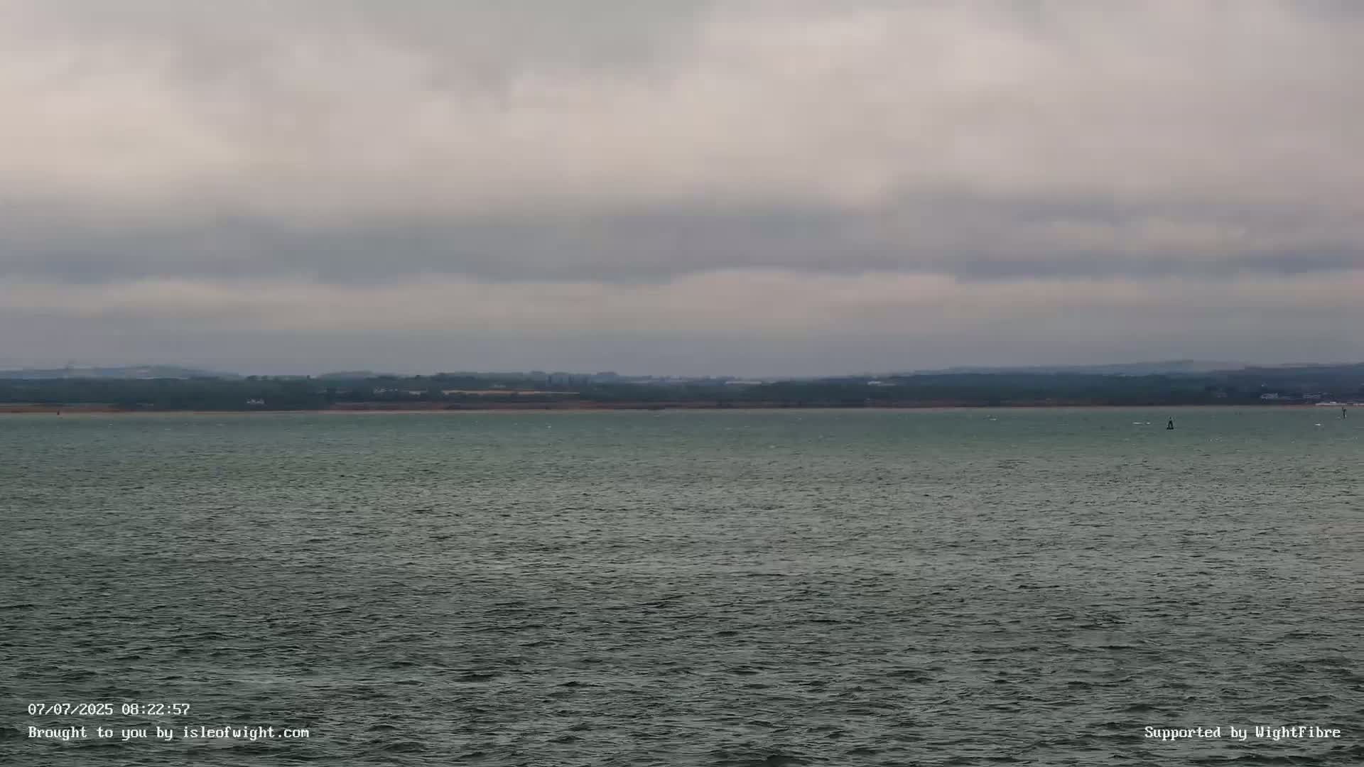 A calm, gray body of water stretches to a distant shoreline under an overcast sky.