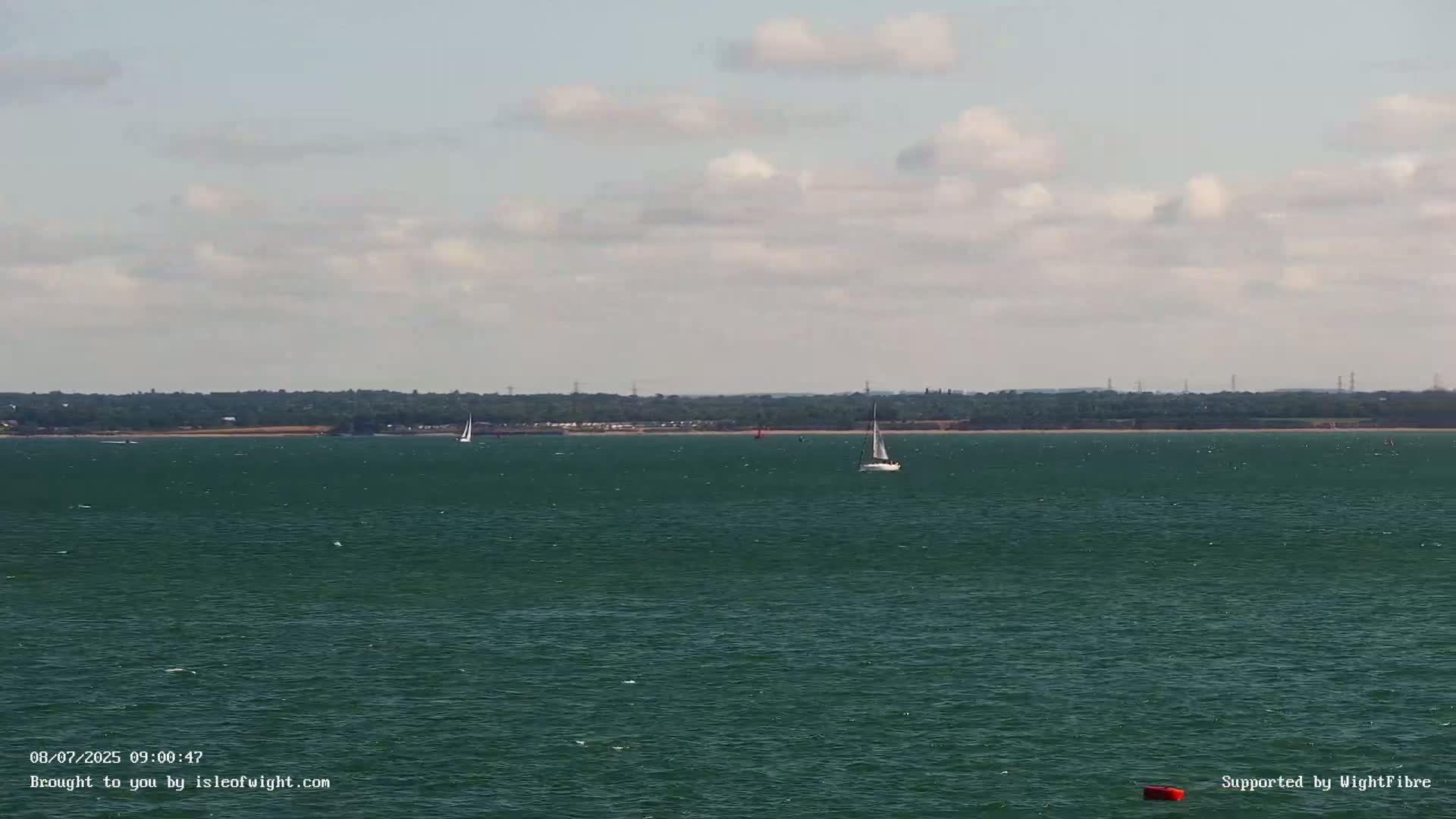 Two sailboats are visible on a dark-green body of water under a partly cloudy sky, with a distant shoreline in the background.