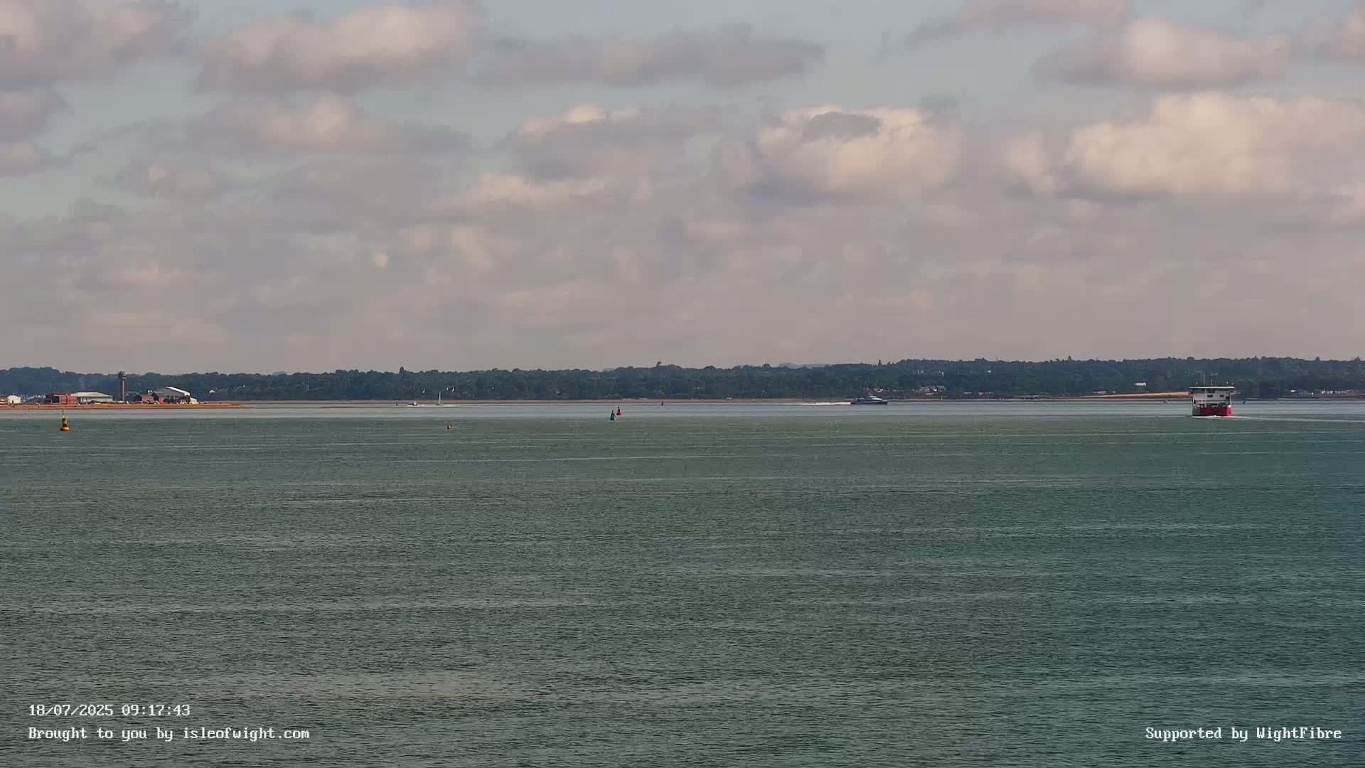 A calm body of water with a few boats and a distant shoreline under a partly cloudy sky.