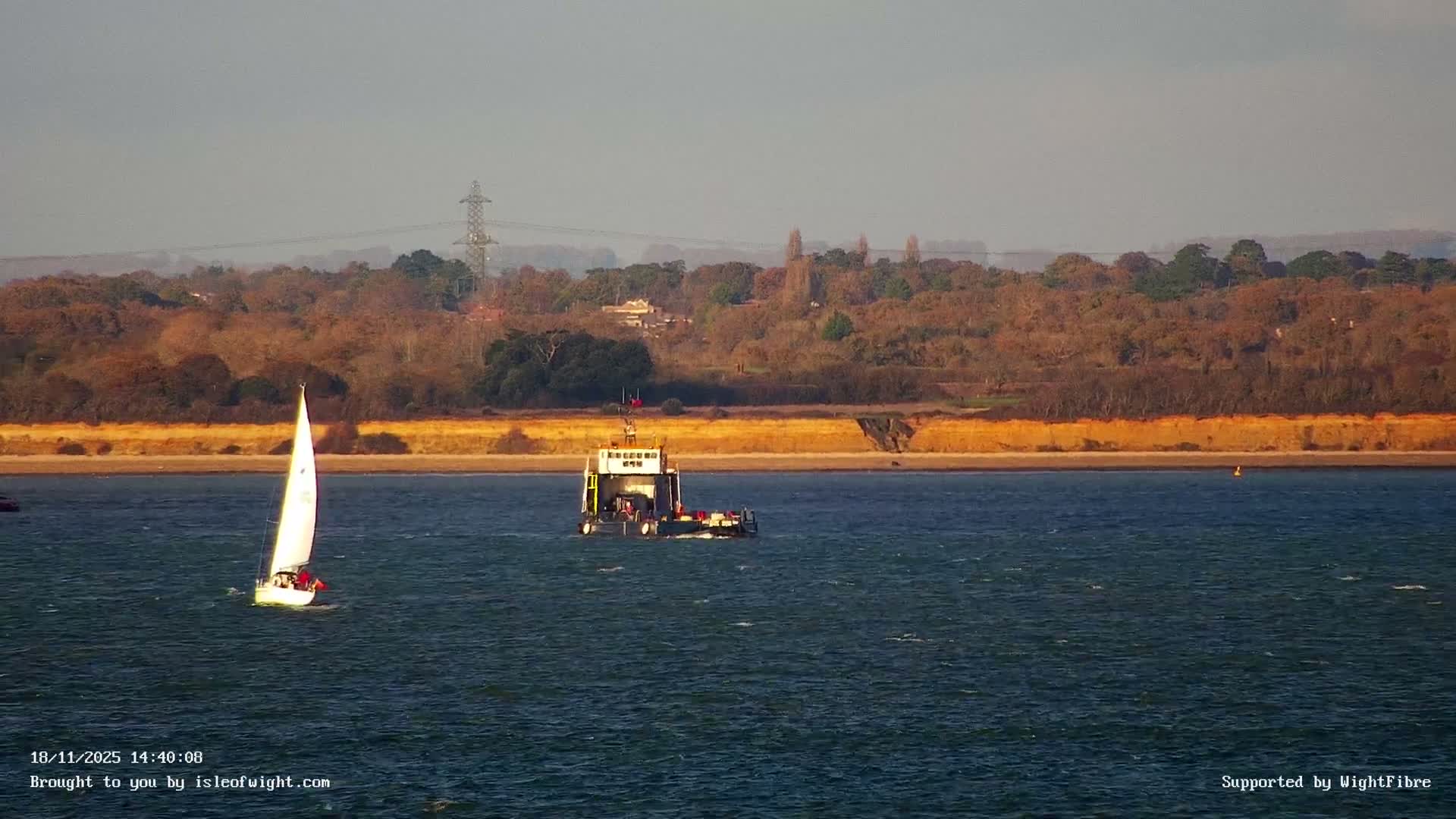 A dark, nighttime scene shows a distant line of lights across a body of water, a lamppost in the foreground illuminating an empty parking lot.