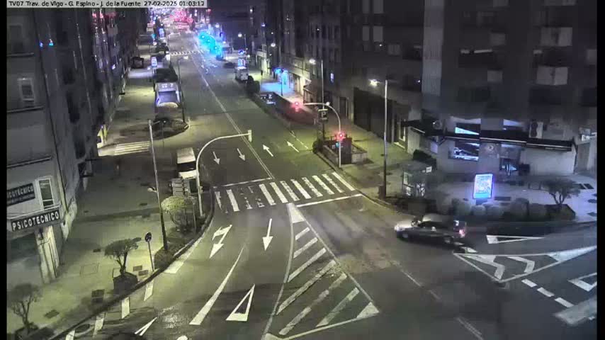 A nighttime street intersection with sparse traffic and buildings lining both sides under clear skies.
