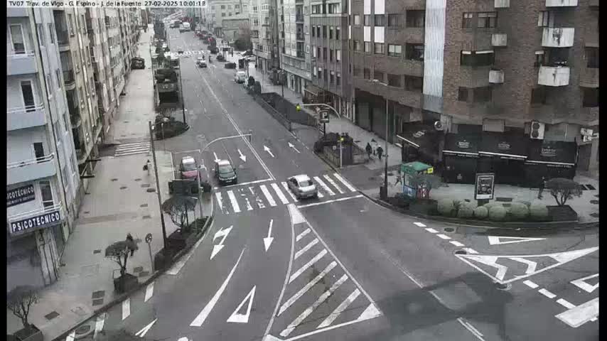 A city street intersection with several cars, pedestrians, and buildings on a cloudy day.