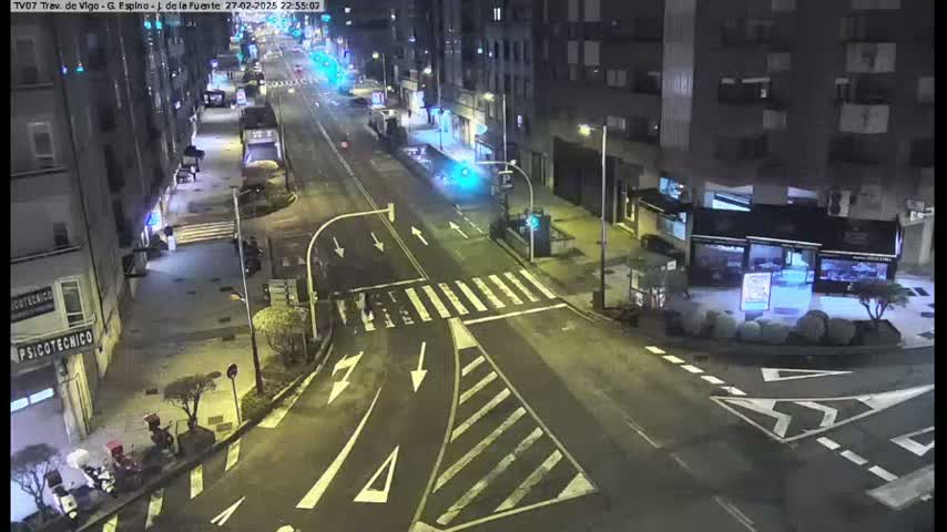 A nighttime view of a city street intersection with light traffic and several buildings along the sides.