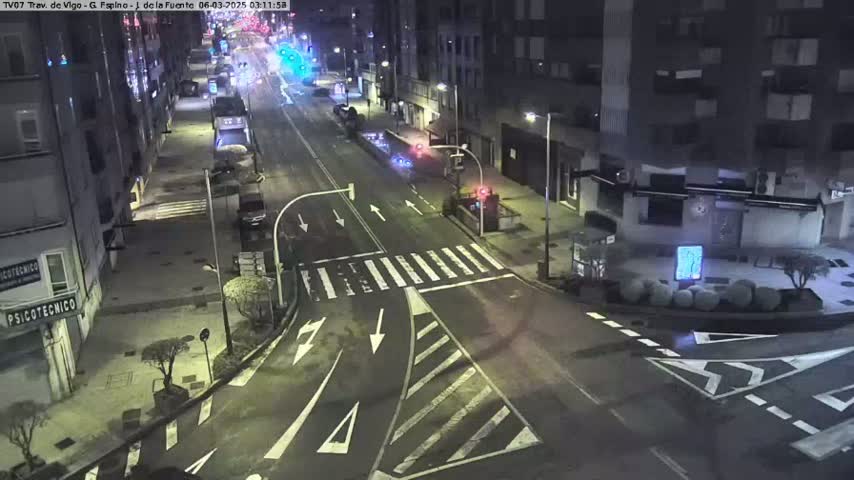 A nighttime, street-level view of a mostly empty intersection with several buildings and streetlights visible.