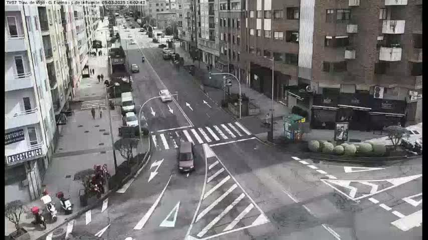 A city street intersection with several vehicles and pedestrians on a cloudy day.