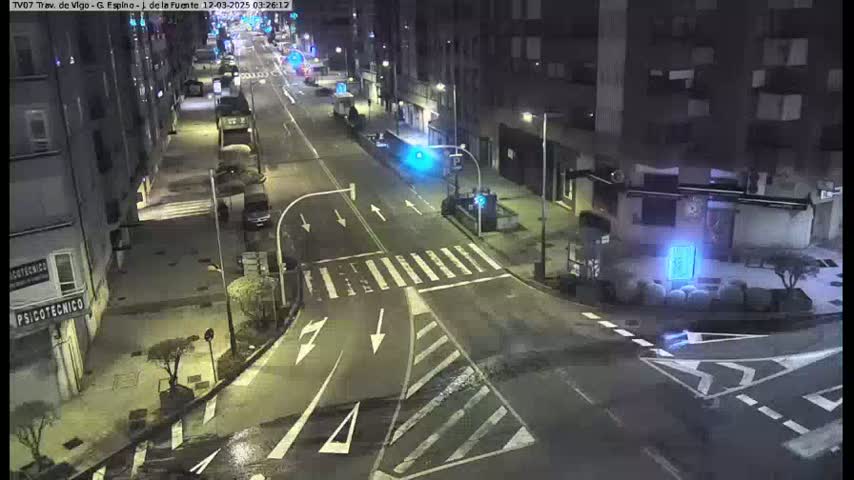 A wet, nighttime street intersection shows sparse traffic with buildings lining both sides of the road.