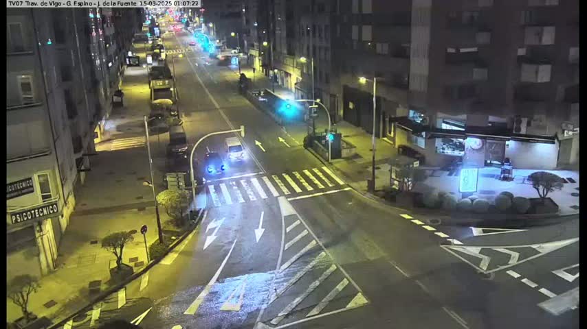 A nighttime, high-angle view of a city street intersection with several cars and buildings visible.