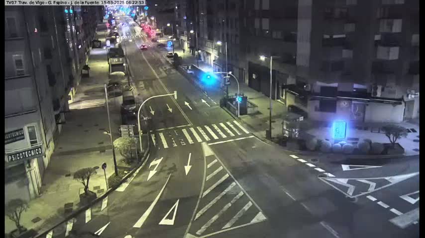 A nighttime street scene shows a mostly empty intersection with buildings lining the streets under streetlights.