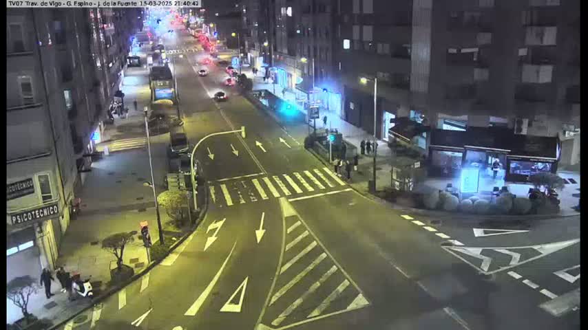 A nighttime street scene shows a multi-lane road intersection with sparse traffic and pedestrians, buildings lining the streets.