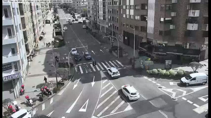 A city street intersection with several cars and pedestrians, on a sunny day.