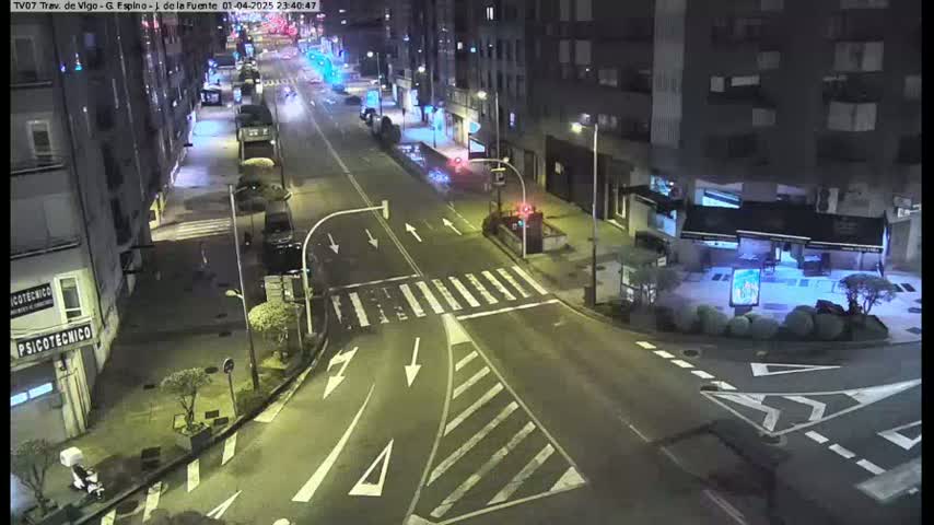 A nighttime street intersection with several buildings and minimal traffic, under dark, clear skies.