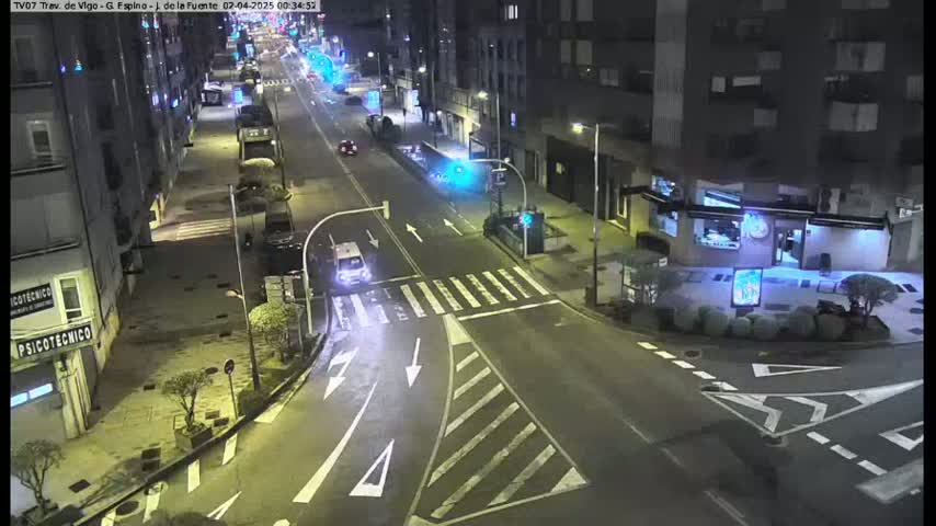 A nighttime street scene shows a sparsely trafficked intersection with buildings lining the sides of the road.