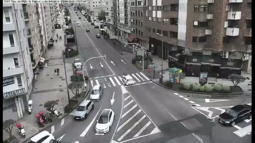 A city street intersection with several cars and pedestrians, on an overcast day.