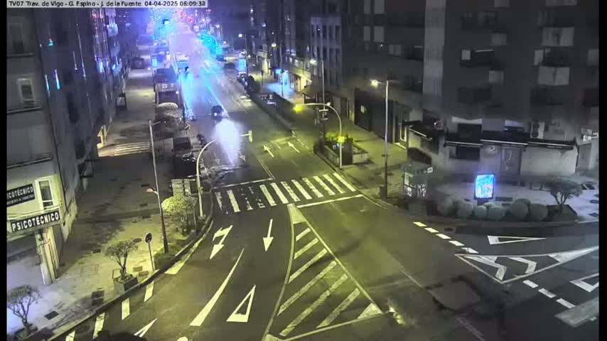 A nighttime view of a street intersection with sparse traffic, under clear skies.