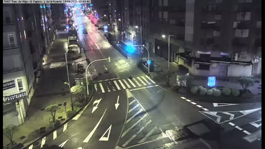 A nighttime street intersection with sparsely trafficked roads, bordered by multi-story buildings under a dark, clear sky.