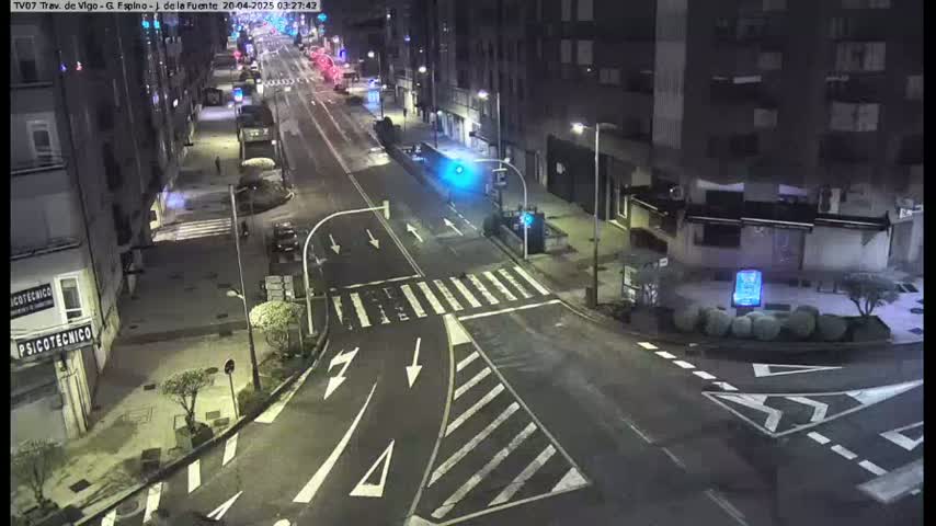A nighttime, empty street intersection with crosswalks and traffic signals, surrounded by multi-story buildings.