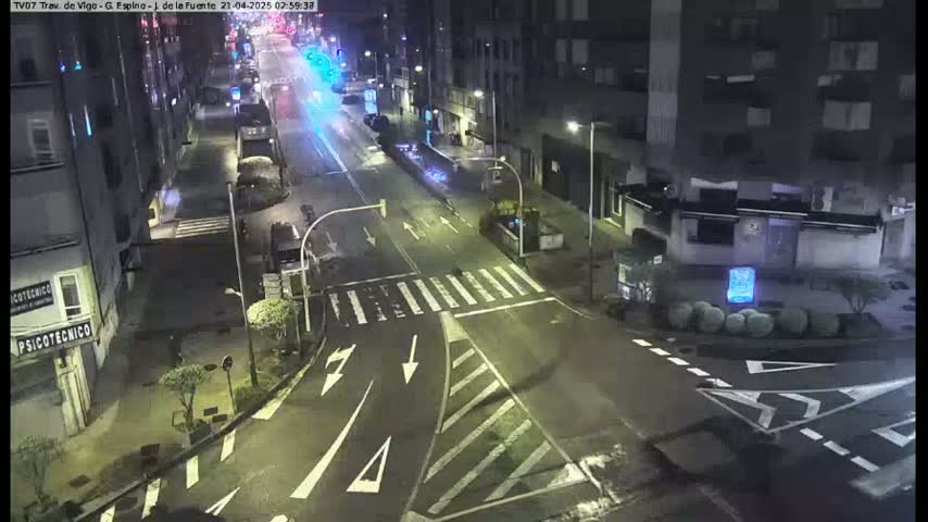 A nighttime street intersection with sparse traffic, showing several buildings and streetlights under clear skies.