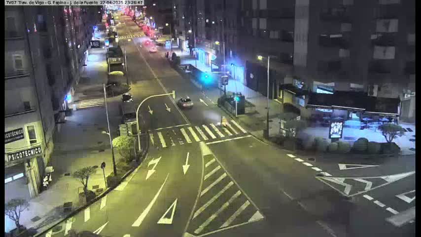A nighttime, street-level view of a city intersection with several cars and buildings, illuminated by streetlights.