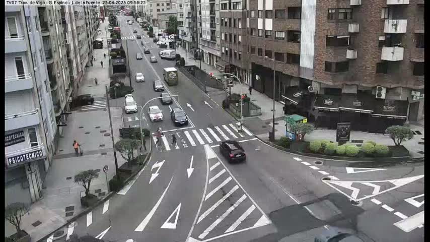 A street intersection in a city, with several cars and pedestrians, on a partly cloudy day.