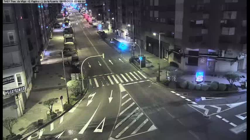 A nighttime street scene shows a mostly empty road with some cars and buildings along the sides, under dark conditions.