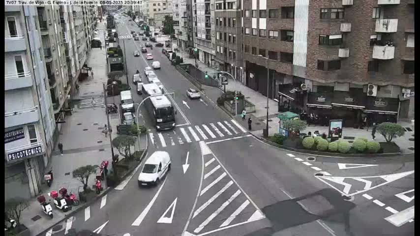 A city street intersection with several vehicles, including a bus and a van, is shown on an overcast day.