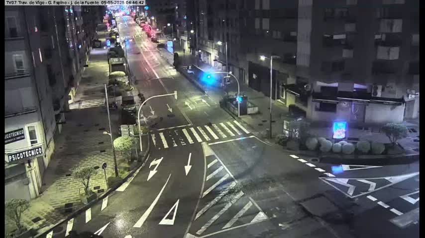 A wet, empty street at night, lined with buildings, shows crosswalks and street markings under dim streetlights.