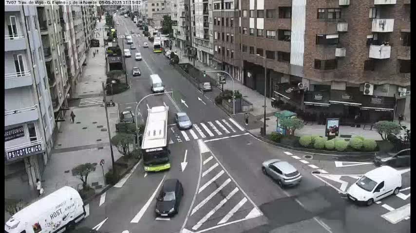 A city street intersection with several cars and a bus, under an overcast sky.