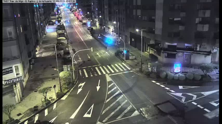 A nighttime street scene shows a mostly empty intersection with several buildings lining the road.
