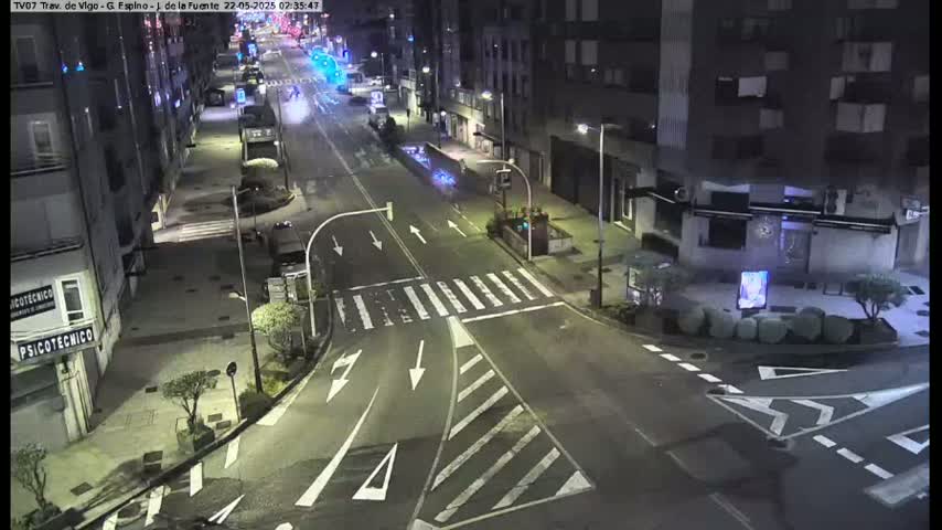 A nighttime, street-level view of a mostly empty intersection with several buildings visible, and minimal vehicle traffic.