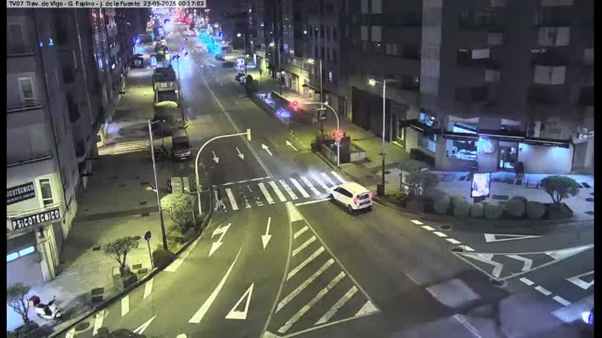 A nighttime street intersection with several cars and buildings, illuminated by streetlights.