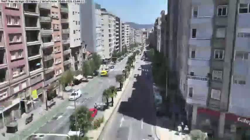 A sunny day reveals a long city street lined with multi-story buildings, sparse traffic, and occasional palm trees.