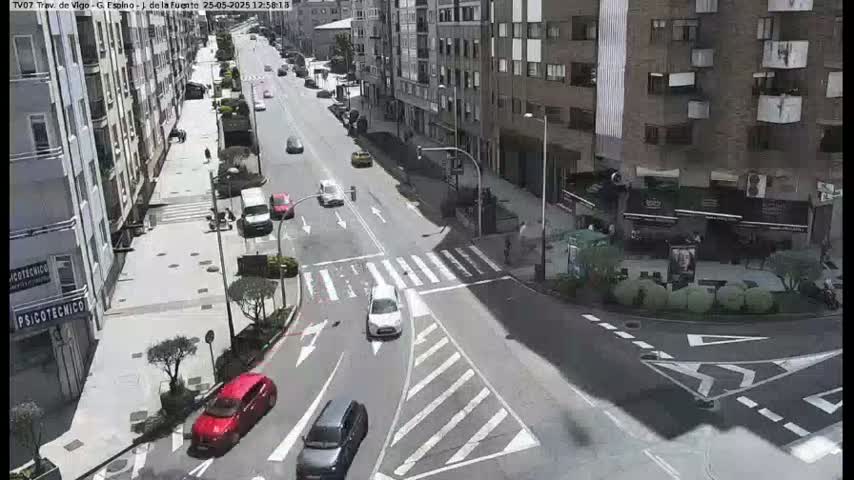 A sunny day street scene shows several cars at an intersection in front of multi-story buildings.
