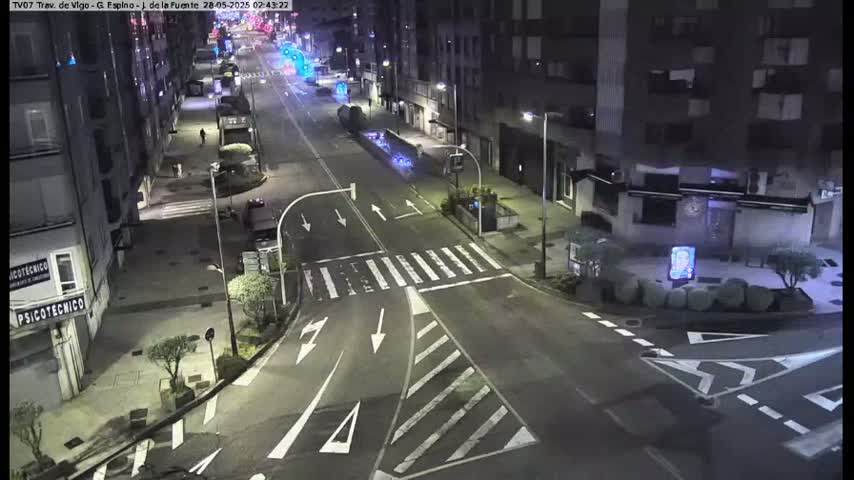A nighttime, high-angle view of a mostly empty street intersection with buildings lining both sides.
