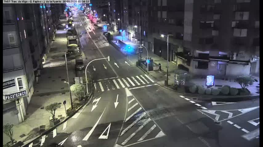 A nighttime, wet street intersection with several cars and buildings visible under streetlights.