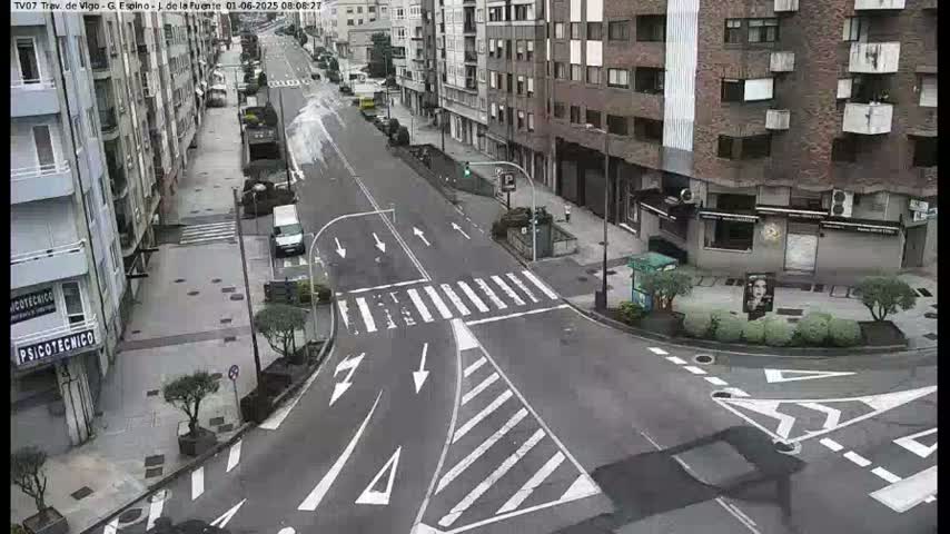 A city street intersection with crosswalks and light poles, under an overcast sky.