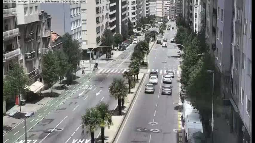 A sunny city street scene shows several cars driving on a multi-lane road lined with buildings and palm trees.