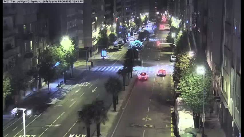 A nighttime, street-level view of a city street with sparse traffic, lined with buildings and palm trees.