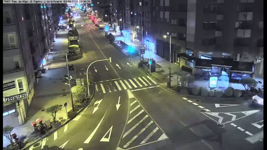 A nighttime street scene shows a mostly empty road intersection with some vehicles and pedestrians, illuminated by streetlights.