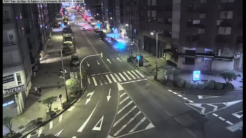 A nighttime aerial view of a city intersection with sparsely populated streets and buildings under clear skies.