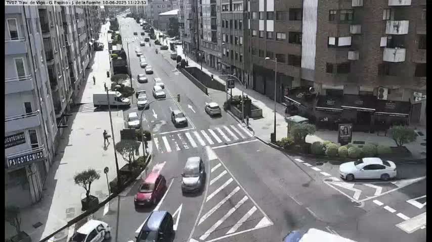 A sunny day view of a city intersection with several cars driving on a multi-lane road.