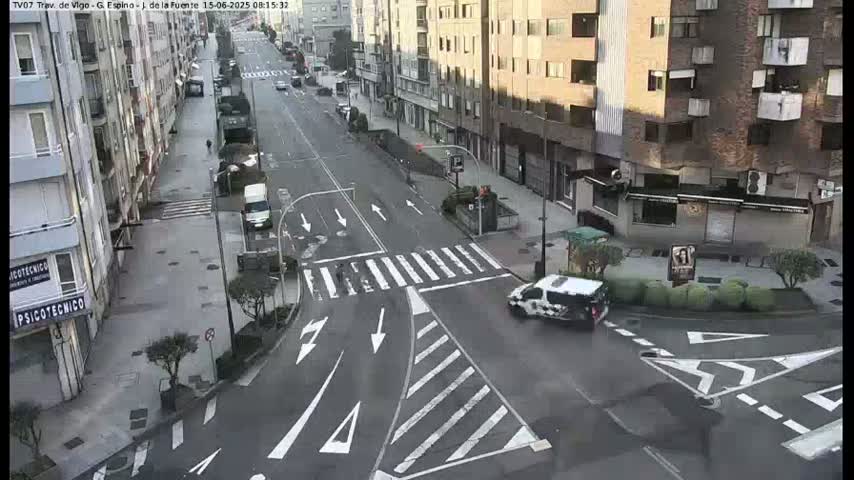 A street intersection in a city, with several cars and a van visible on a mostly clear day.