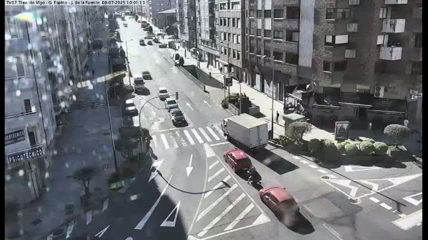 A sunny day reveals a city street scene with several cars at a crosswalk and a truck parked nearby, all surrounded by multi-story buildings.