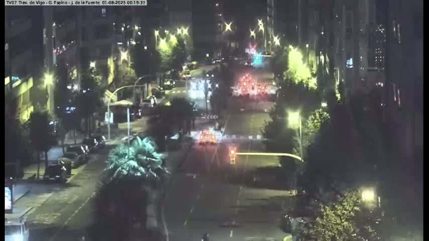 A nighttime, overhead view of a city street with cars and some pedestrians, illuminated by streetlights and building lights.