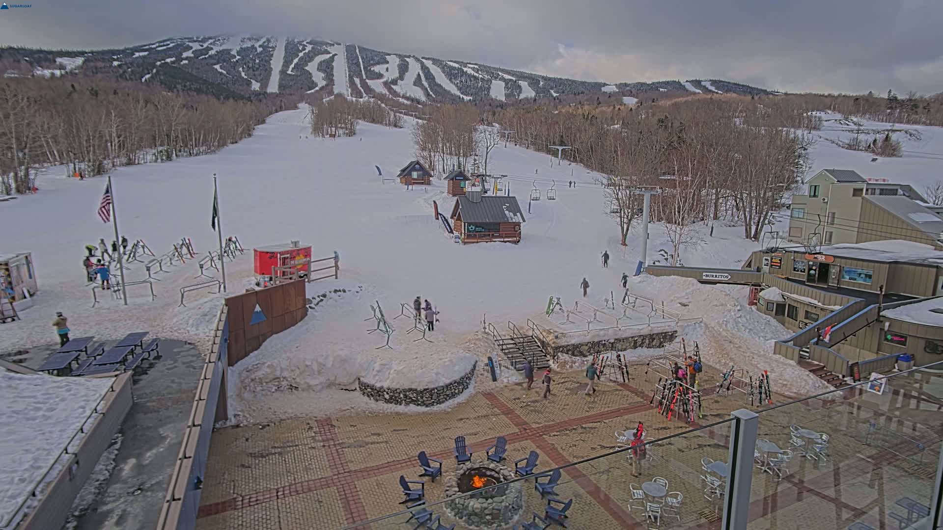 A snow-covered ski resort with several buildings, ski lifts, and people enjoying the overcast day.