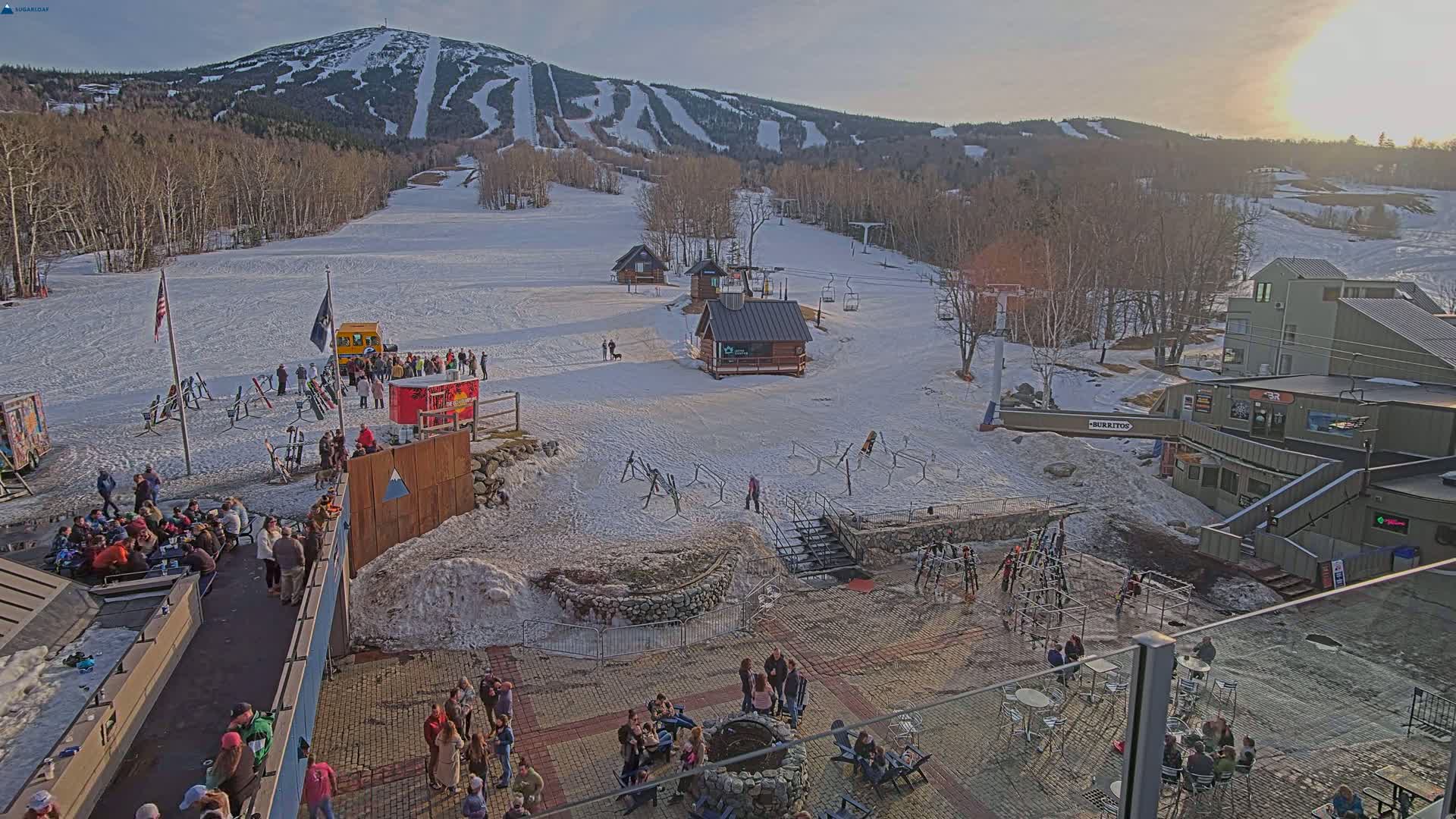 A snow-covered ski resort with a mountain in the background, under a partly sunny sky.
