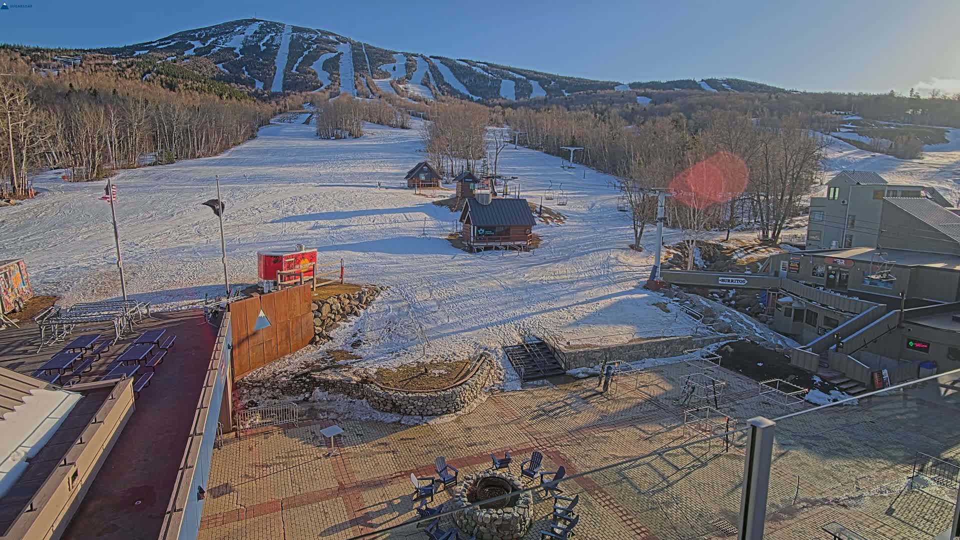 A snow-covered ski resort with several small buildings and a large mountain in the background on a sunny day.