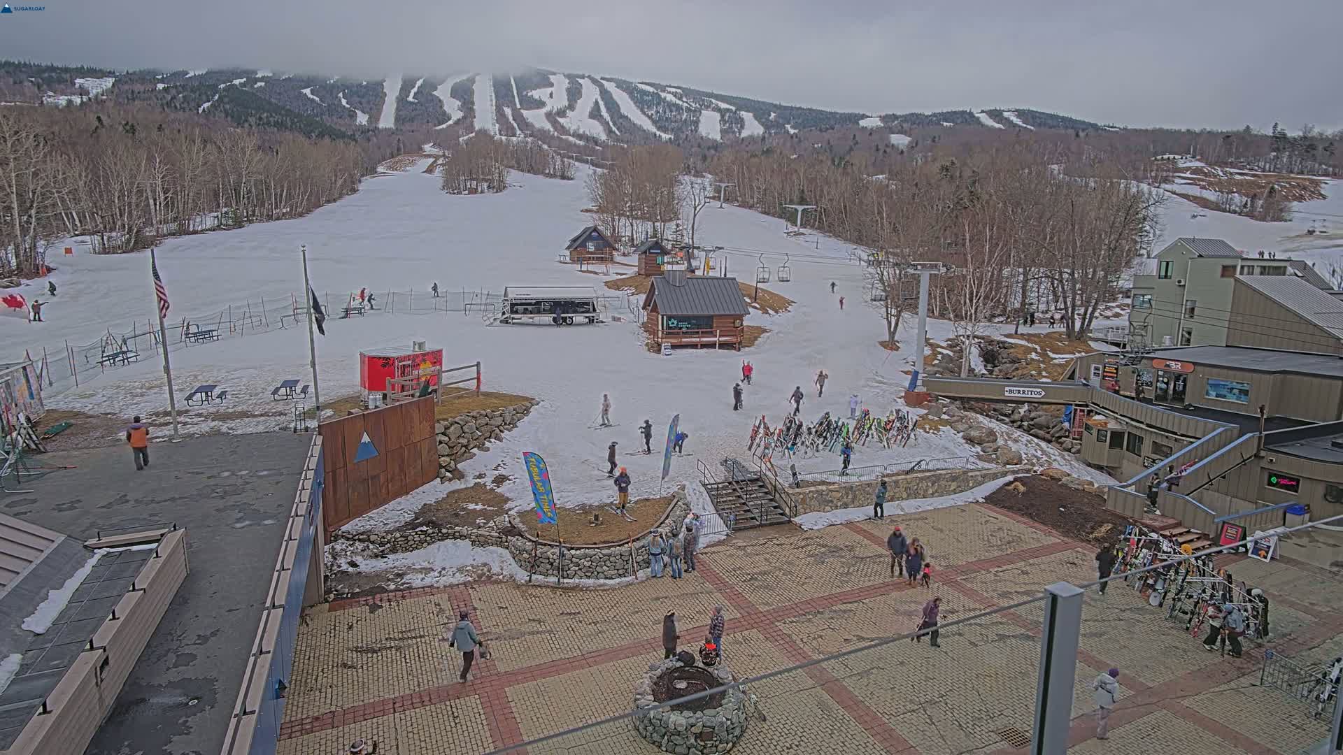 A ski resort base area with snow-covered slopes and several people, under an overcast sky.