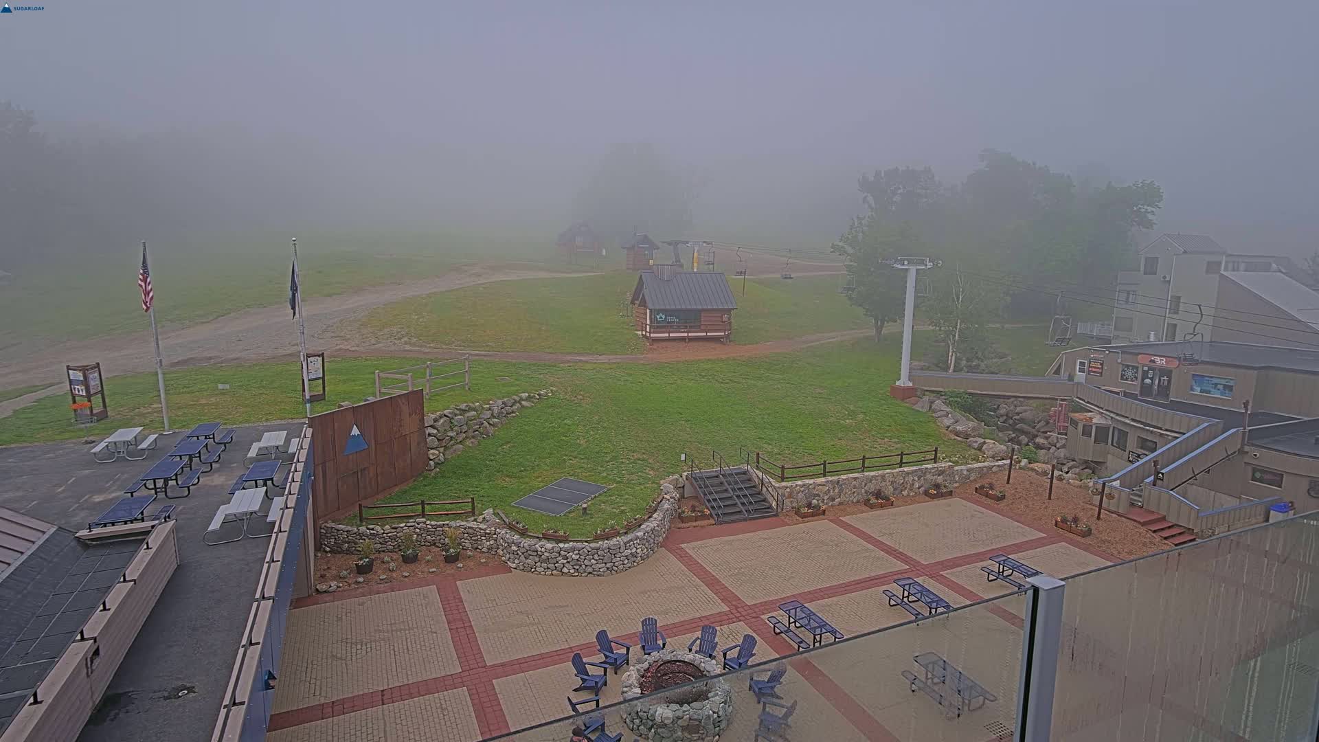 A foggy outdoor patio area with picnic tables, a fire pit, and a ski lift in the background.